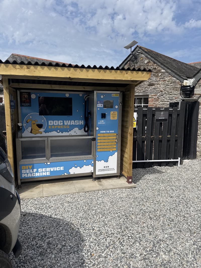 The outdoor self-service dog wash station under its timber shelter on the gravel yard beside the stone building
